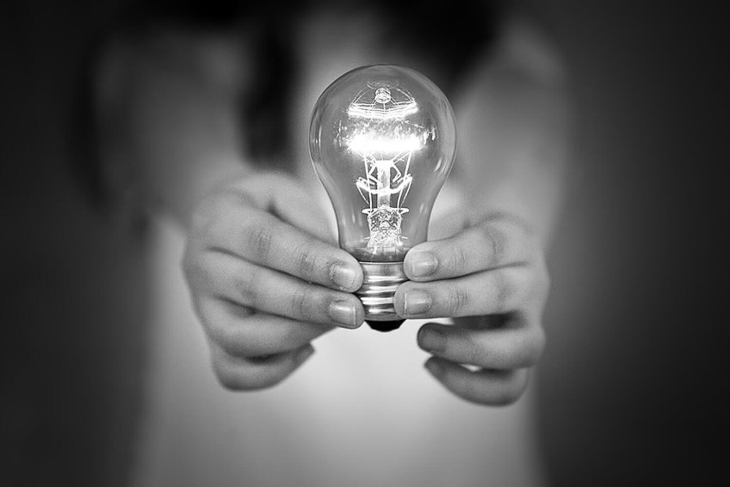 Black and white photo of a lighted bulb held in a child's hands