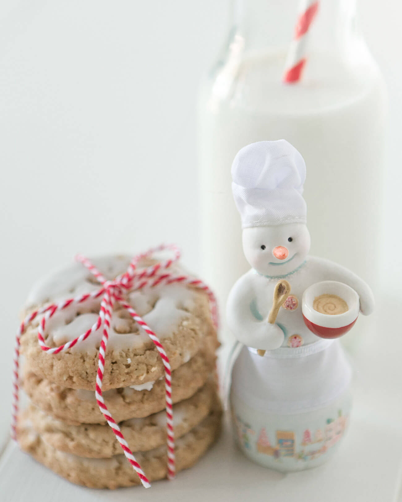 Photo of oatmeal cookies tied together with red and white twine, a china snowman, and a bottle of milk
