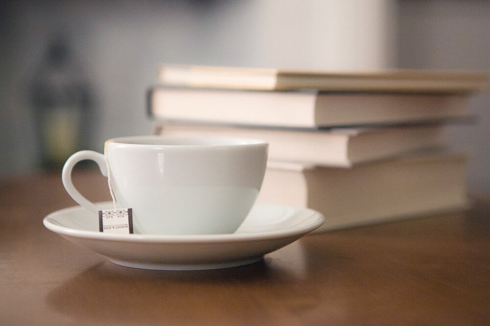 Stack of neutral colored books beside a white china teacup