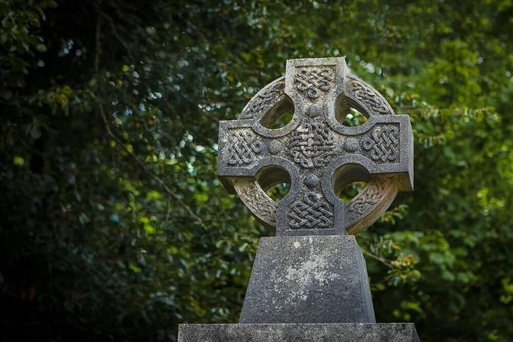 Photo of a gray stone celtic cross in front of green leaves