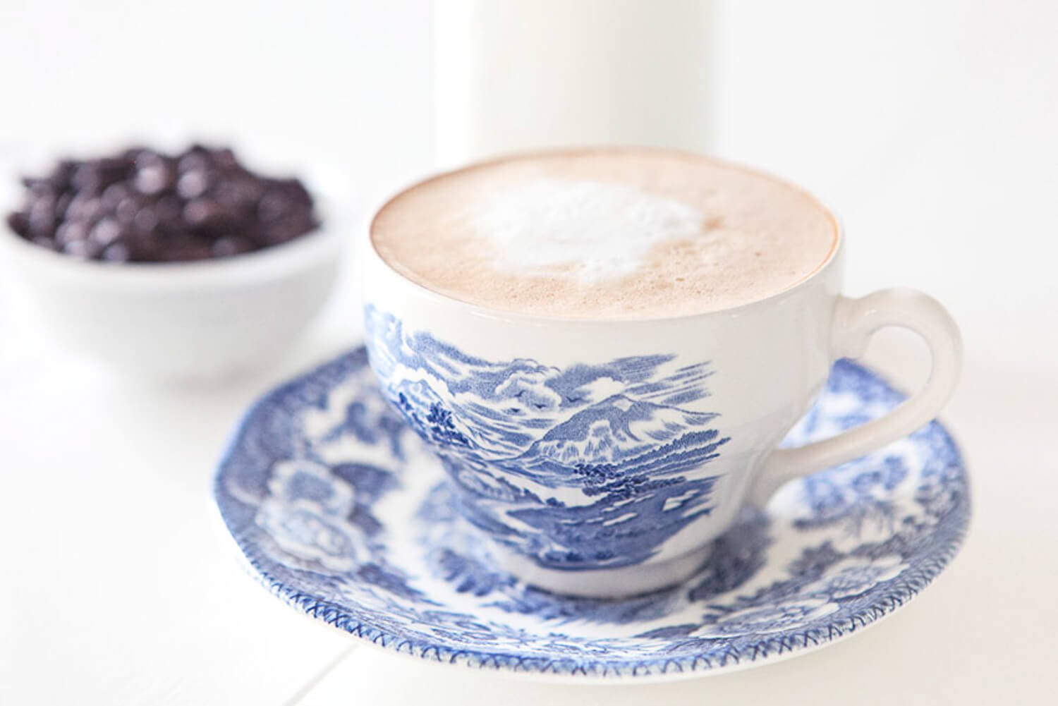 Photo of coffee in a blue and white china cup and saucer with coffee beans in the background
