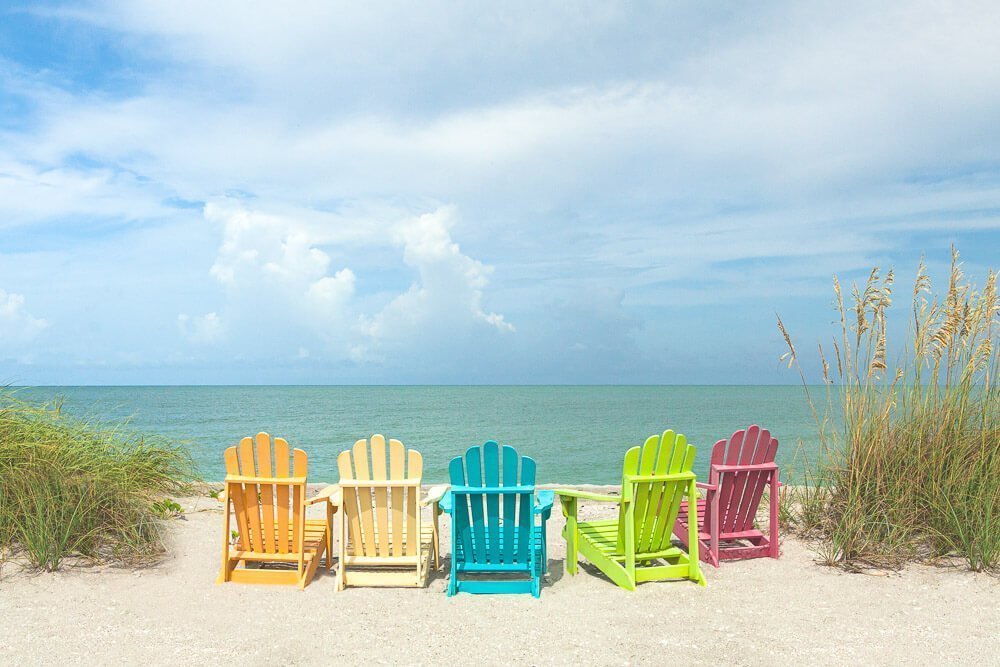 Photo of five colorful beach chairs between clumps of sea oats on the beach under a blue sky