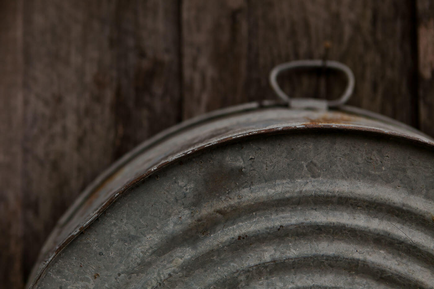Photo of a rusy washtub hanging on the side of a weathered barn
