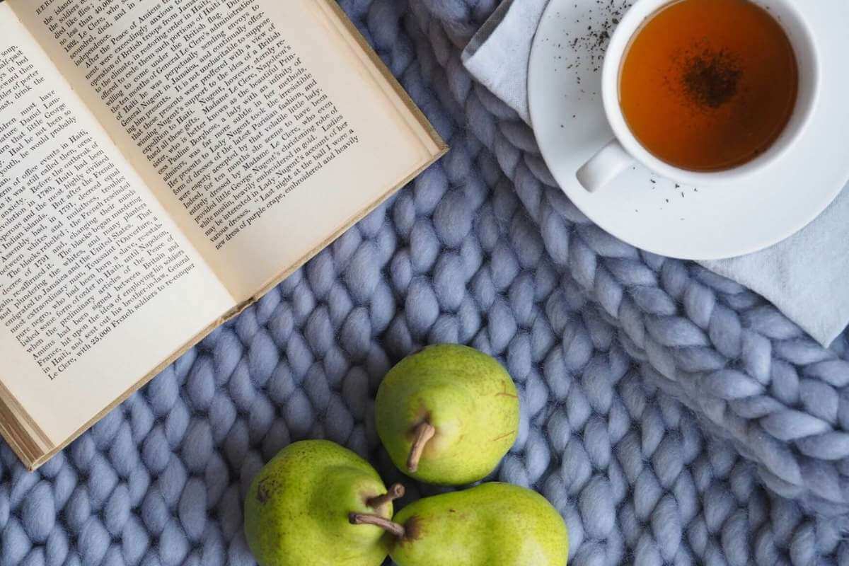 Photo of a book, cup of tea, and three pears on a blue blanket